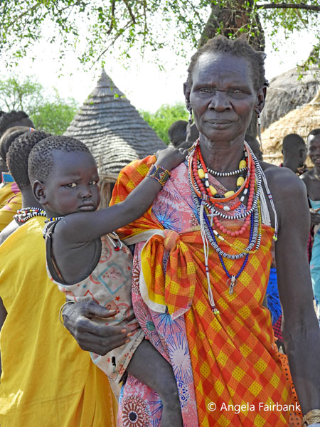 older Toposa woman in checked yellwo and red cloth with child on hip